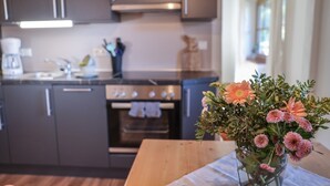 A modern kitchen with dark cabinets, a stainless steel range hood, and a wooden table with a vase of flowers.