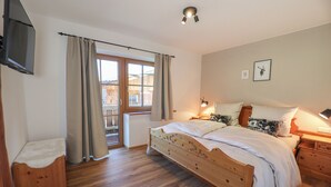 A bedroom with a wooden bed, a TV mounted on the wall, and a window with curtains.