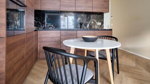 A modern kitchen with wooden cabinets, a black marble countertop, and a round dining table with two chairs.