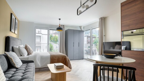 Una habitación de hotel moderna con cama, sofá, mesa de comedor y un balcón con vistas.
