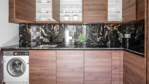 A kitchen with wooden cabinets, a built-in washing machine, and a marble backsplash. - Premium Wiedikon 2BR w/ Storage & W/D, nr Transport, by Blueground (Zurich)