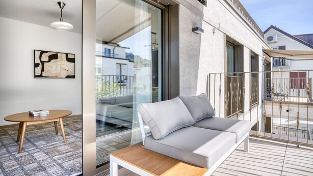 A modern balcony with a grey sofa, a small round table, and a ceiling light. - Premium Wiedikon 2BR w/ Storage & W/D, nr Transport, by Blueground (Zurich)