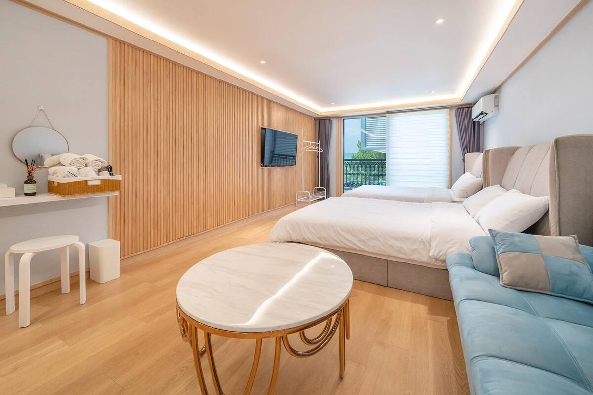 A modern hotel room with a large bed, a sofa, a small round table, and a TV mounted on the wall.