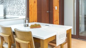 A modern kitchen with a white countertop, wooden chairs, a wooden door, and a glass door. - Donghae Badae Meomuleuda (Donghae)