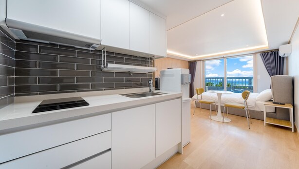 A modern kitchen with a black tiled backsplash, a built-in stove, and a compact refrigerator. - Donghae Badae Meomuleuda (Donghae)