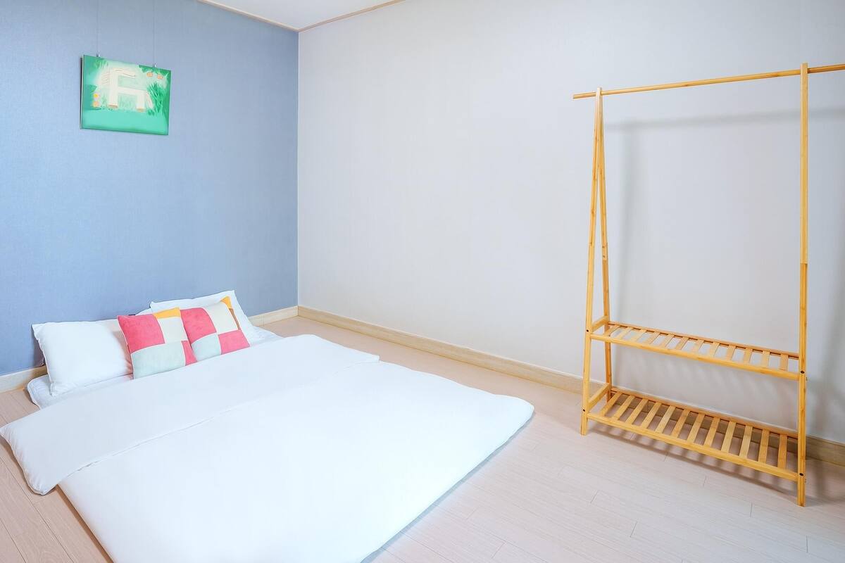 A bedroom with a bed, pillows, a wooden drying rack, and a wall-mounted picture.