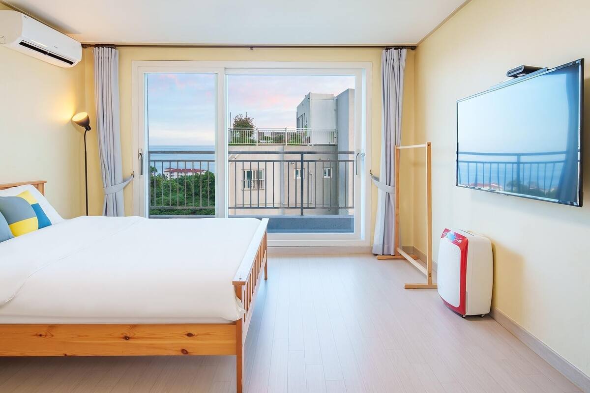 A bedroom with a bed, a TV, a radiator, and a balcony with a view.