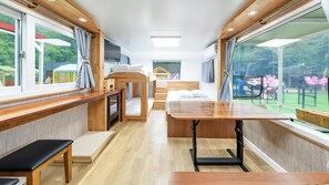 A compact, modern RV interior with a wooden bench, a table, and a bed.