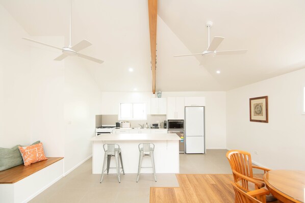 A modern kitchen with white cabinets, a central island with bar stools, and two ceiling fans. - 2 bedrm, 2 bathrm house w/patio includes car (Kingston)