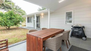 A covered patio with a wooden table and wicker chairs, a grill, and a Weber grill. - Garden View Cottage(2 Bedroom,2 Bathroom) (Kingston)