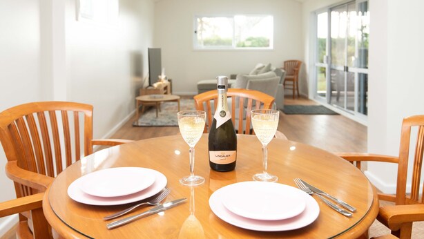 A dining table with pink plates, a bottle of Lindauer wine, and two glasses of wine. - Garden View Cottage(2 Bedroom,2 Bathroom) (Kingston)