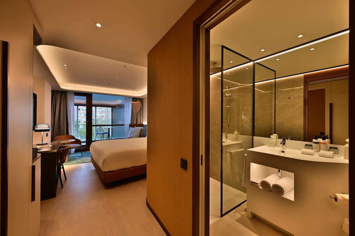 Una habitación de hotel moderna con cama, escritorio y zona de ducha con paredes de vidrio.
