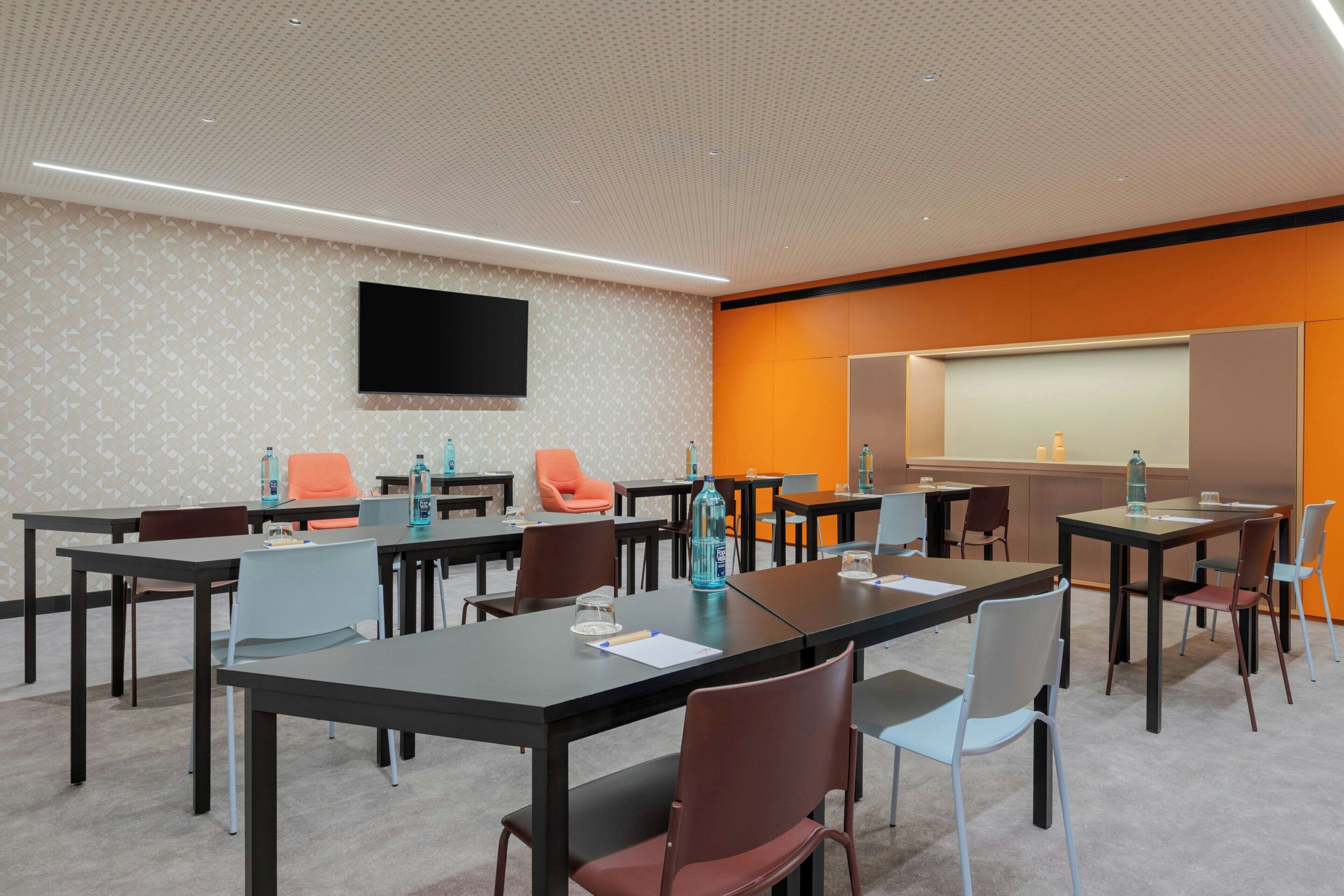 A conference room with tables, chairs, a flat-screen TV, and a projection screen.