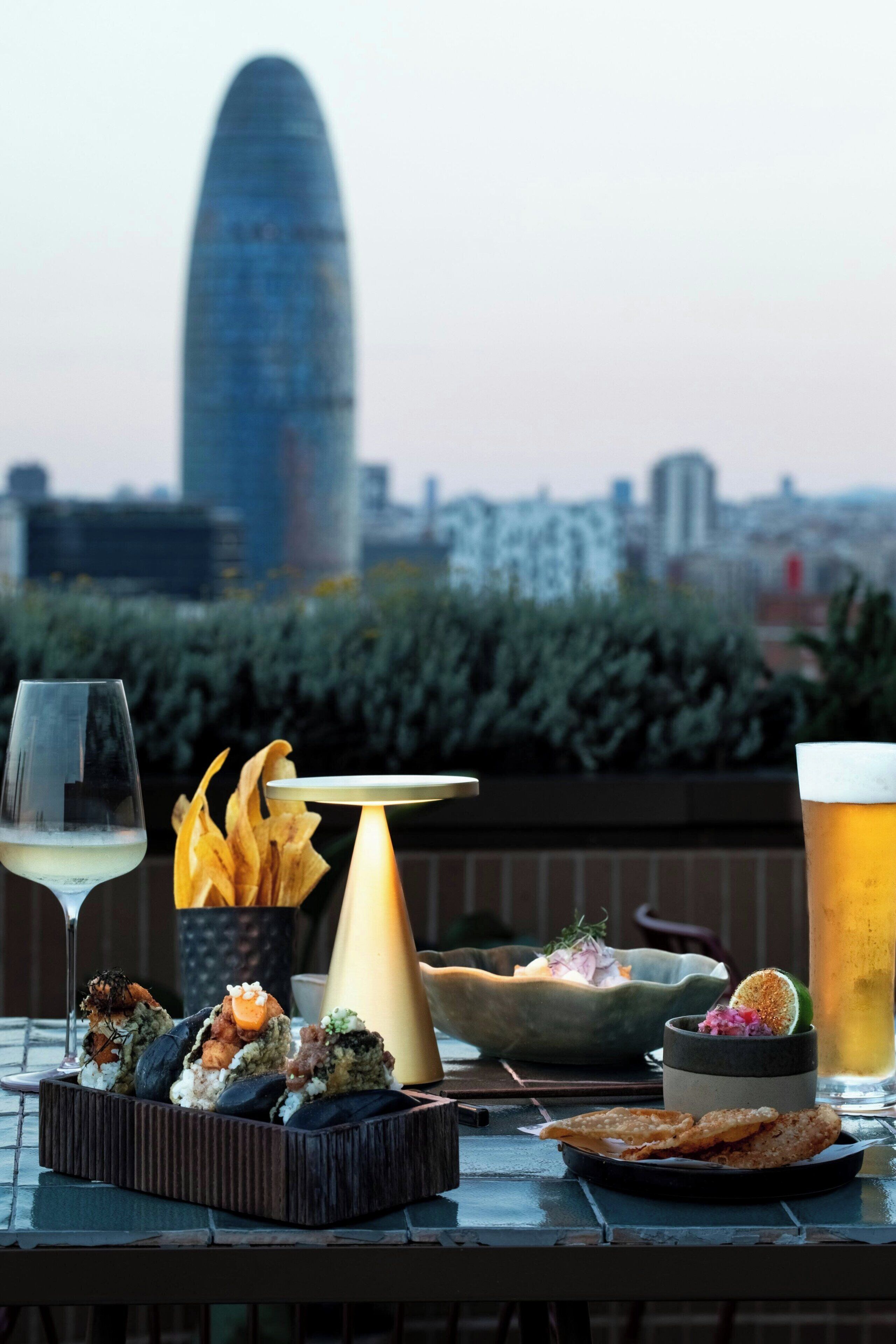 A table with food and drinks, a city skyline in the background, and a building with a pointed top.
