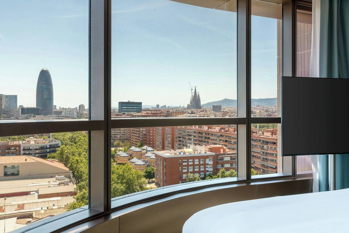 Ein Hotelzimmer mit großem Fenster und Blick auf die Stadt, einschließlich eines markanten Gebäudes und Wohngebiete.