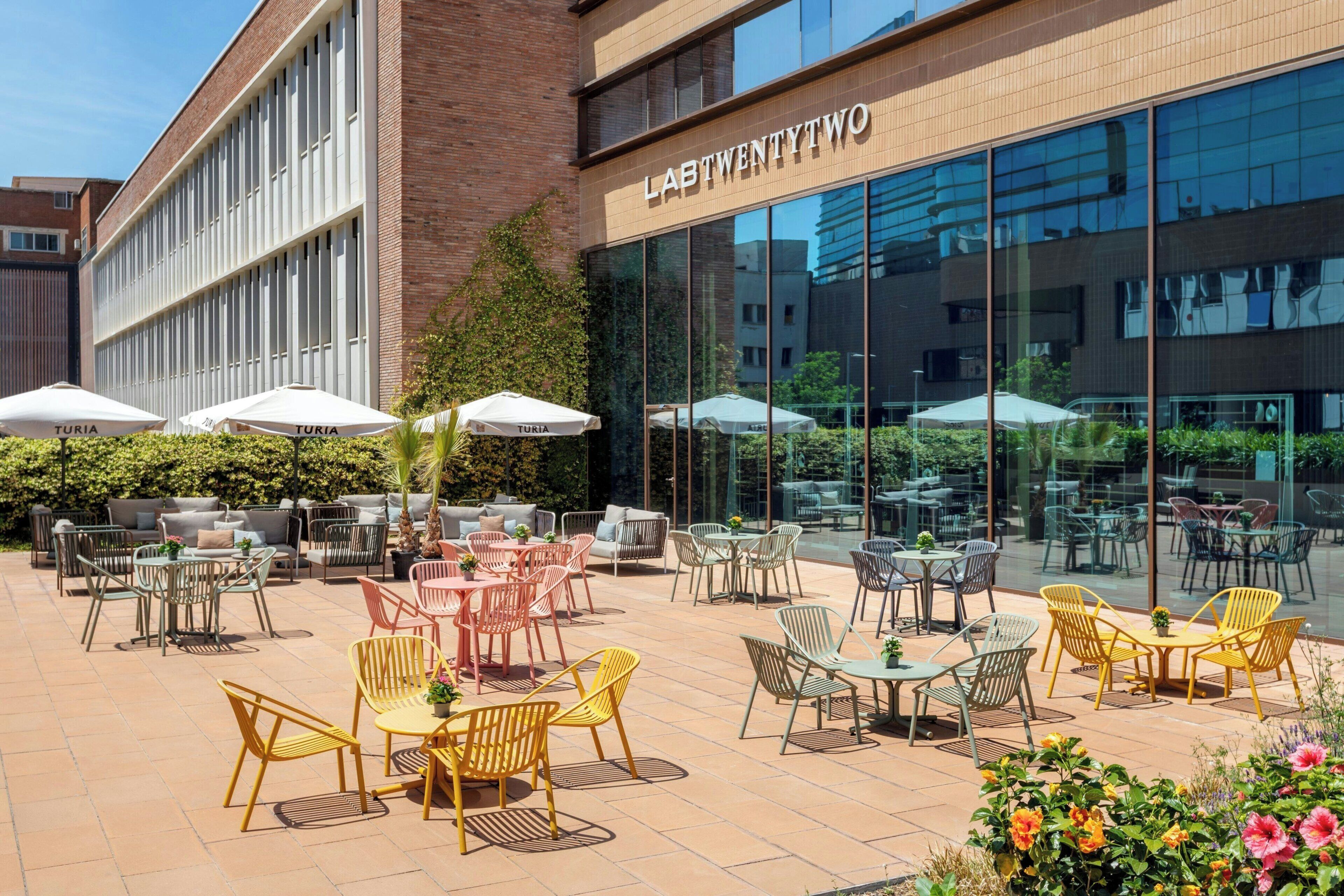 Un edificio moderno con un letrero que dice 'LASTTWENTY TWO' y un patio al aire libre con diferentes distribuciones de asientos y sombrillas.