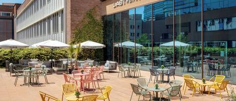 Un edificio moderno con un letrero que dice 'LASTTWENTY TWO' y un patio al aire libre con diferentes distribuciones de asientos y sombrillas.