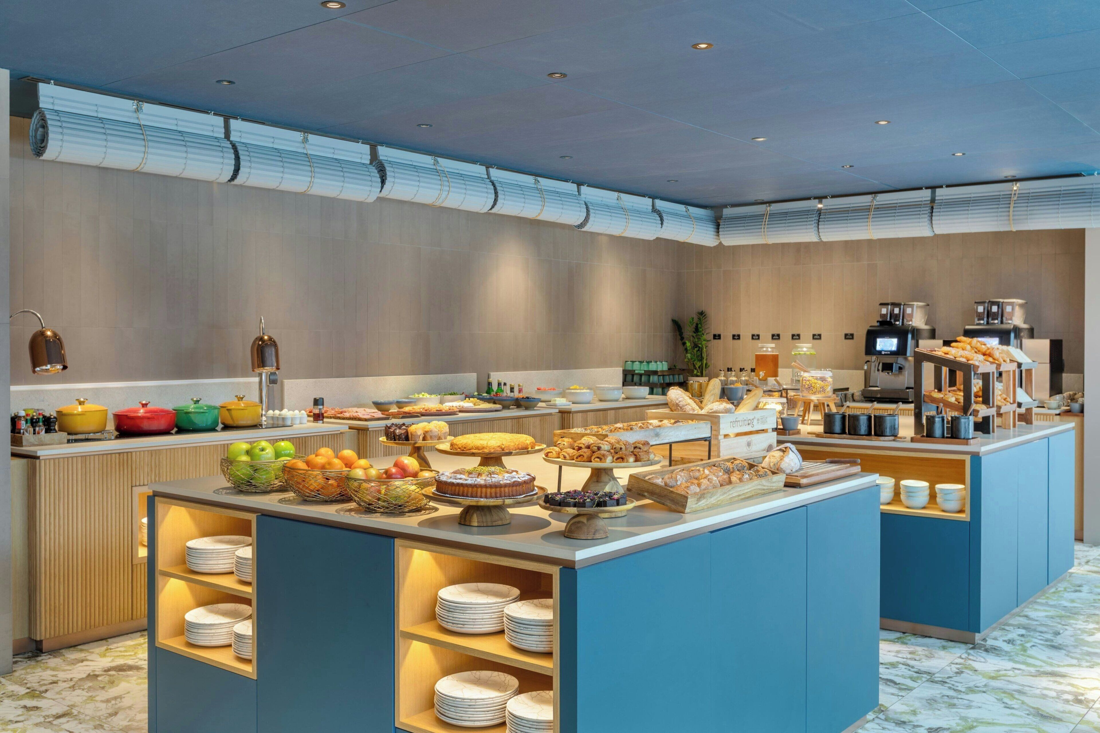 A hotel breakfast area with a buffet setup, including various food items and a coffee station.