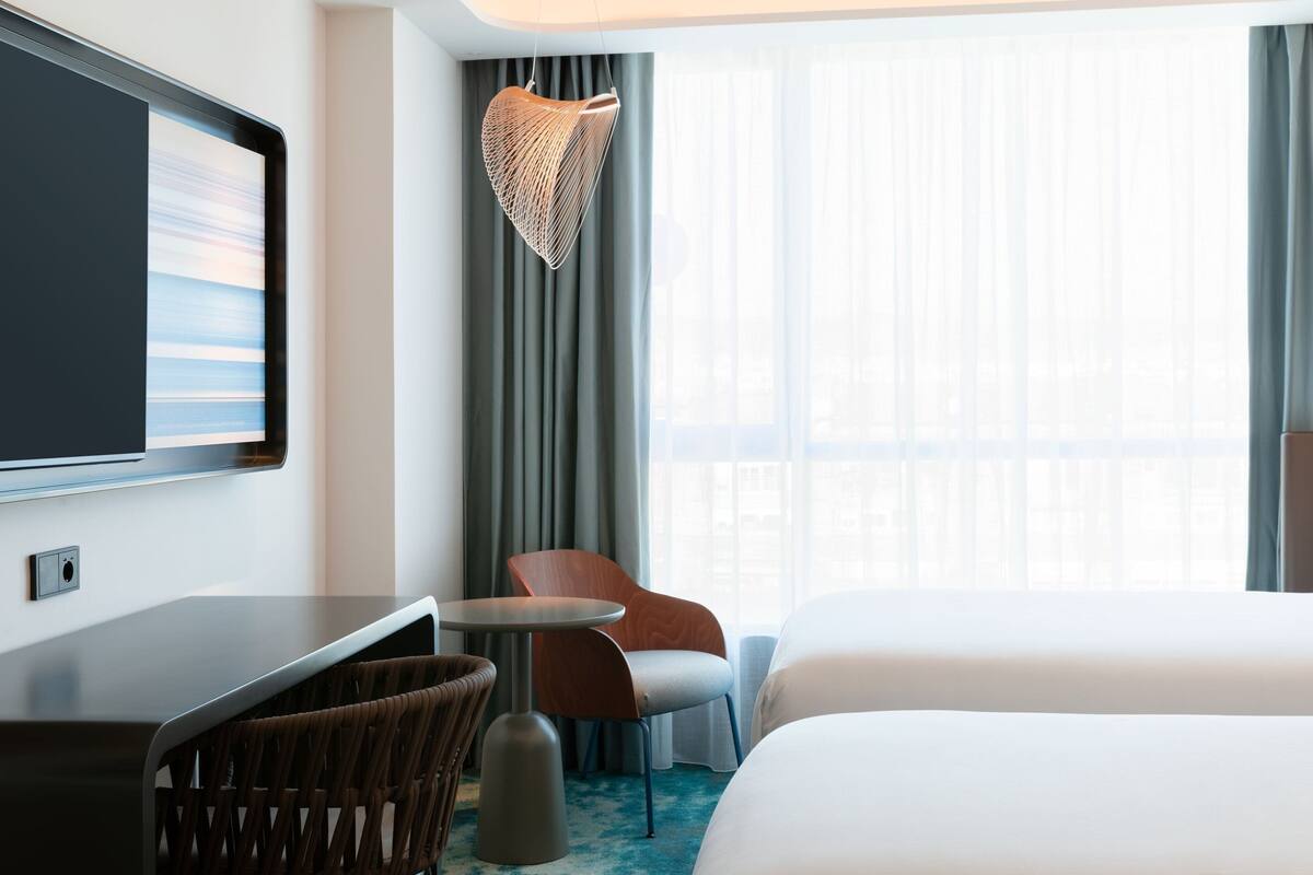 Ein Hotelzimmer mit Bett, Schreibtisch, Stuhl, Fernseher und einem Fenster mit Vorhängen.