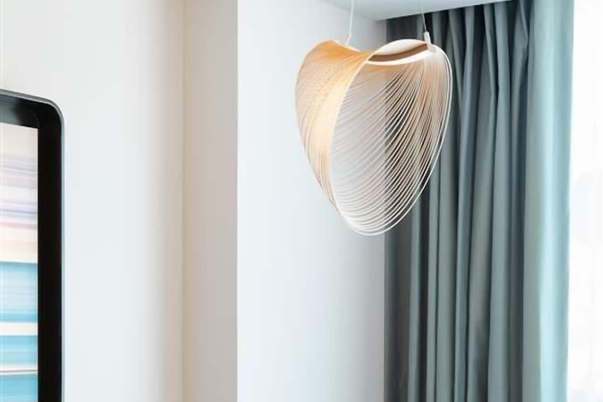 Una habitación de hotel con una cama, una mesa redonda, una silla de madera, una lámpara colgante y una ventana con cortinas.