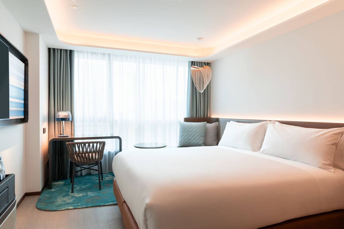Ein Hotelzimmer mit einem großen Bett, einem Schreibtisch mit Stuhl, einem Fernseher und Blick ins Freie.
