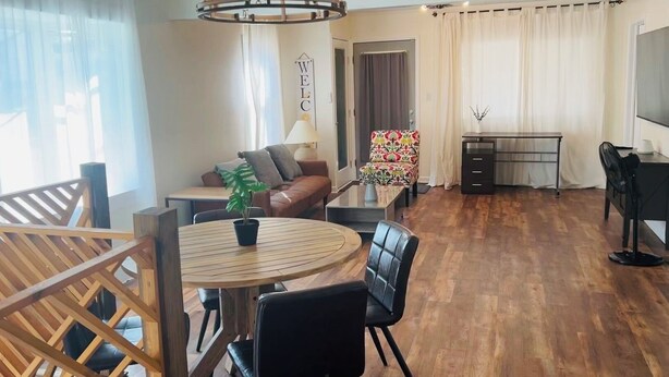 Een moderne woonkamer met een eetgedeelte, houten vloeren, een kroonluchter, een bank, een salontafel en een televisie.