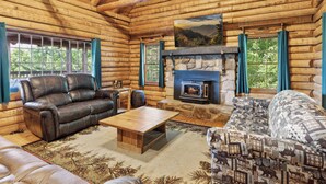 A log cabin interior with a stone fireplace, leather sofas, and a large window with curtains. - 4BD Rustic Log Cabin With Incredible Deck and View! (Gatlinburg)