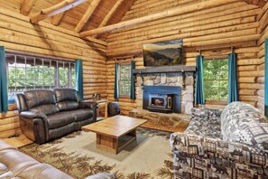 A log cabin interior with a stone fireplace, leather sofas, and a large window with curtains. - 4BD Rustic Log Cabin With Incredible Deck and View! (Gatlinburg)