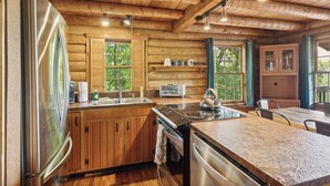 A wooden cabin interior with a kitchen featuring a refrigerator, stove, and sink. - 4BD Rustic Log Cabin With Incredible Deck and View! (Gatlinburg)