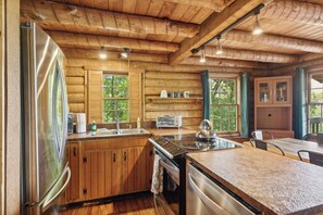 A wooden cabin interior with a kitchen featuring a refrigerator, stove, and sink. - 4BD Rustic Log Cabin With Incredible Deck and View! (Gatlinburg)
