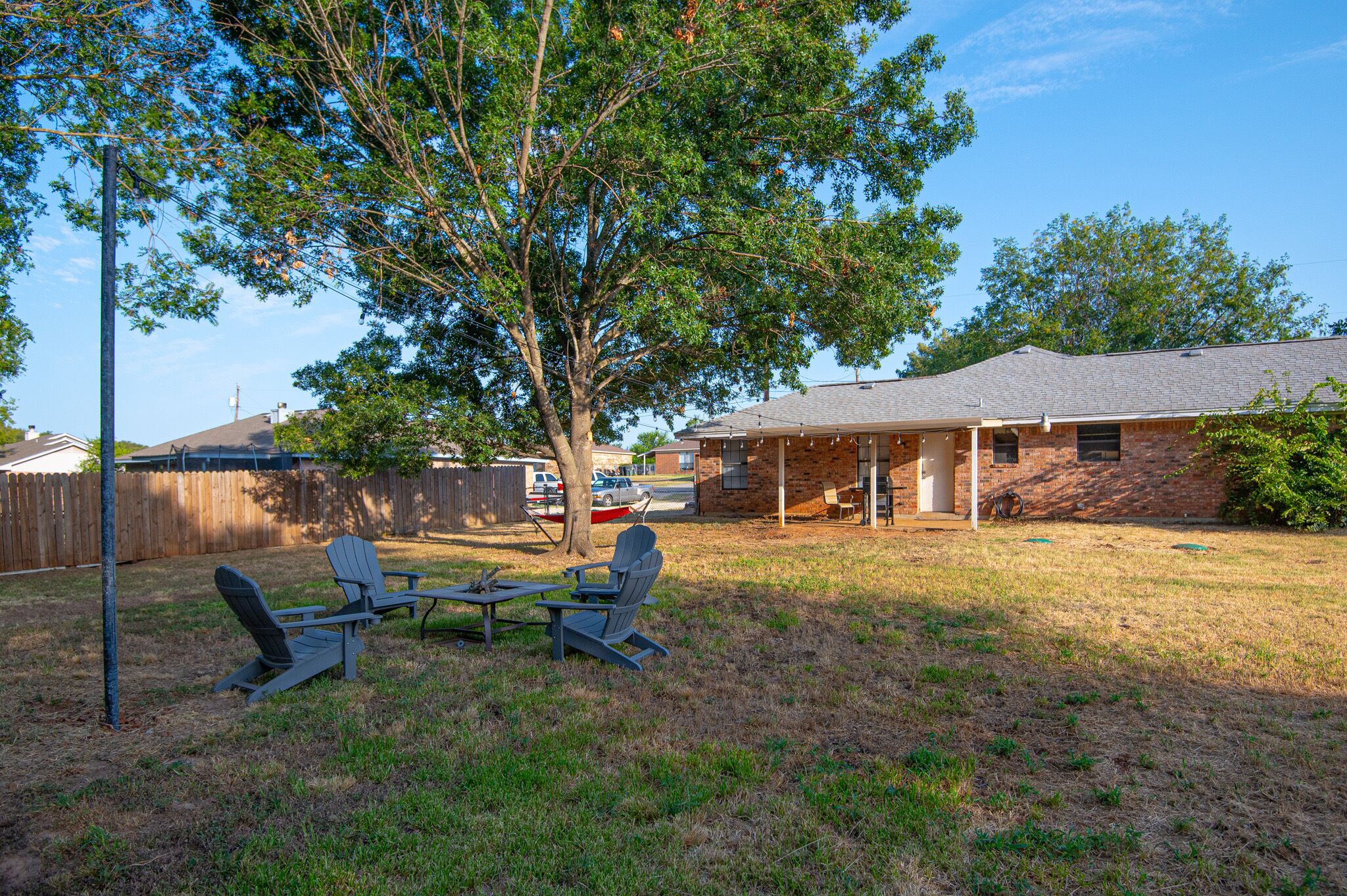 A backyard with two Adirondack chairs, a picnic table, and a tree.