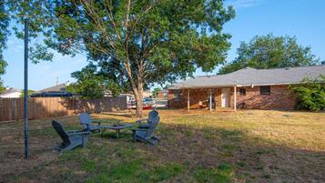 A backyard with two Adirondack chairs, a picnic table, and a tree.
