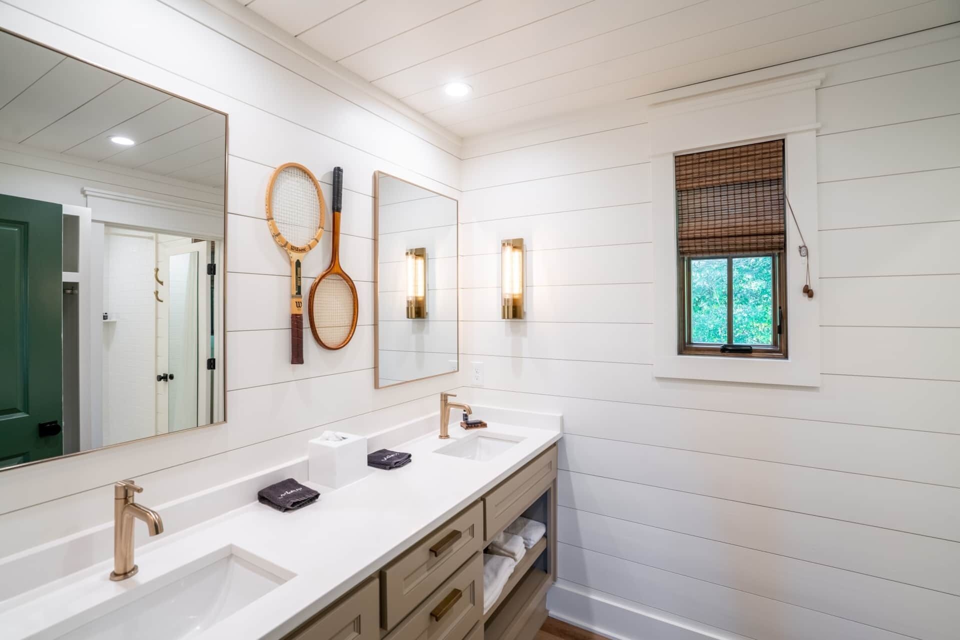 A bathroom with two sinks, a large mirror, and tennis rackets hanging on the wall.