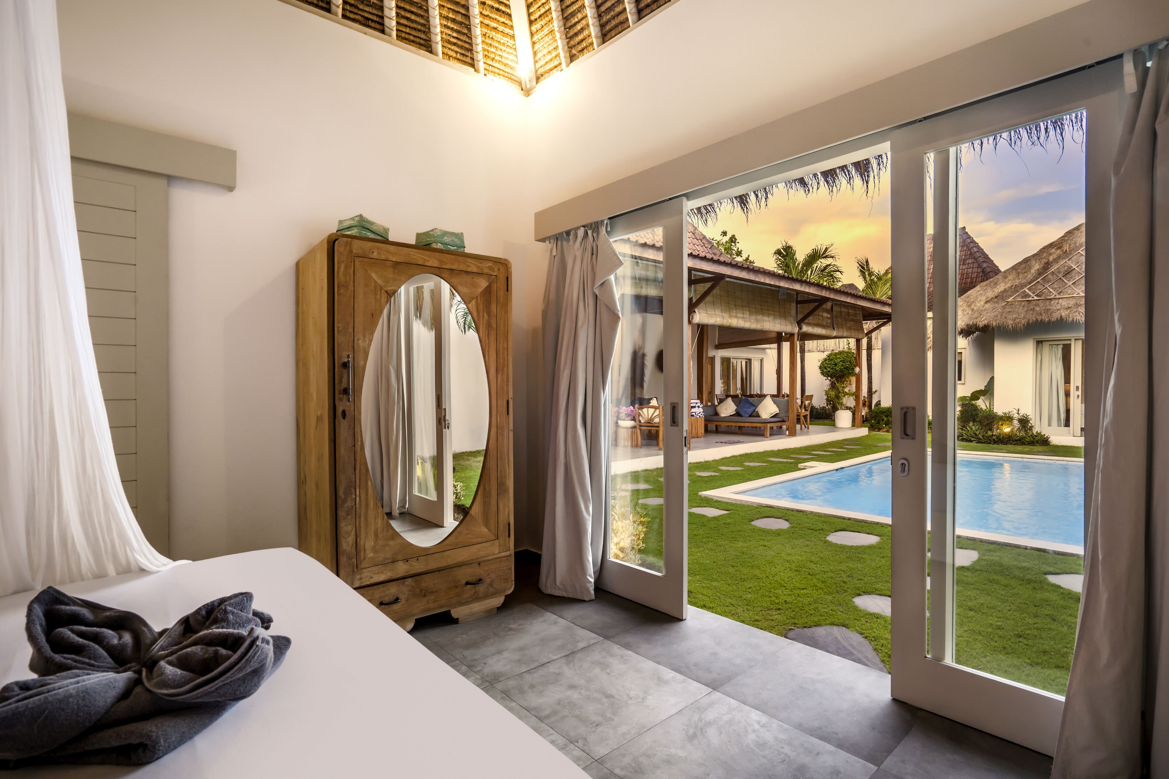 A bedroom with a large bed, a wooden wardrobe, and a sliding glass door leading to a pool area.