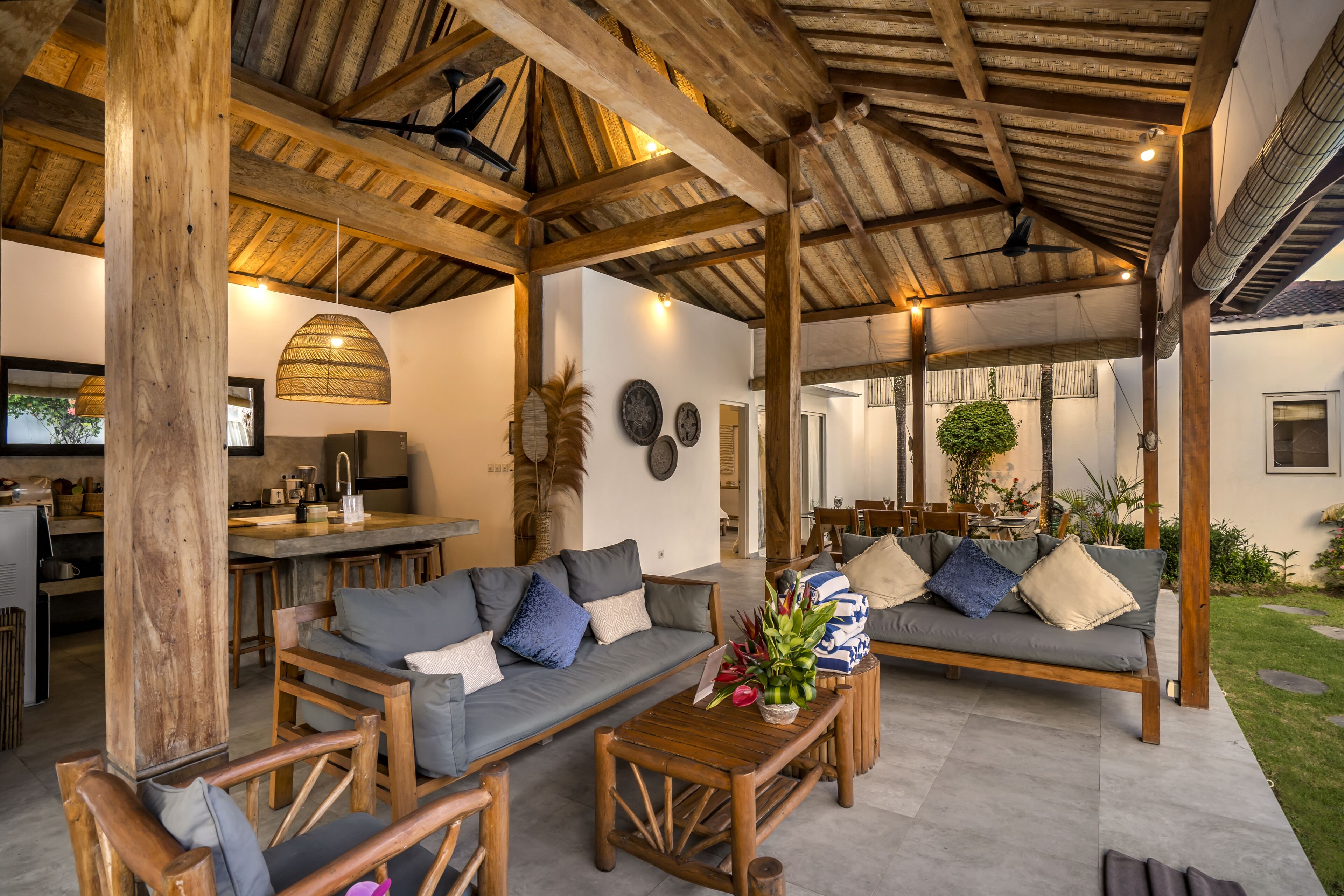 Un espacio de estar techado al aire libre con muebles de madera y una cocina al fondo.