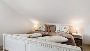A bedroom with a white bed, floral bedding, two bedside tables with lamps, and a wooden floor. - Holiday Apartment 'Kirsche' with Wi-Fi (Sasbach am Kaiserstuhl)