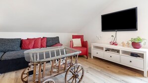 Ein Wohnzimmer mit einer Couch, einem roten Sessel, einem an der Wand montierten Fernseher, einem hölzernen Couchtisch und einem weißen Konsolentisch mit Schubladen.