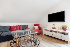 A living room with a sofa, a red chair, a TV mounted on the wall, a wooden coffee table, and a white console table with drawers. - Holiday Apartment 'Kirsche' with Shared Terrace, Shared Garden and Wi-Fi (Sasbach am Kaiserstuhl)