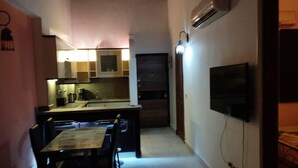 A narrow hallway with a dining area featuring a table and chairs, a kitchen with cabinets and appliances, and a mounted television on the wall. - 2-Bed property in Makadi Heights (MAKADI BAY)