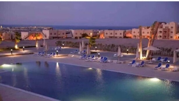 A swimming pool with lounge chairs and umbrellas, surrounded by buildings with warm lighting. - 2-Bed property in Makadi Heights (MAKADI BAY)