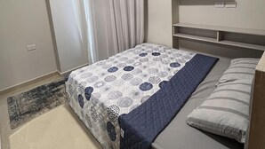 A bedroom with a bed, a nightstand, a shelf with a plant, and a window with curtains. - Charming 1-Bed Chalet in Hurghada (Hurghada)