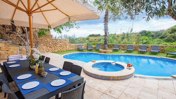A poolside area with a hot tub, dining table set with plates, and lounge chairs. - Villa Soldanis Sleeps 12 with Pool (Xaghra)