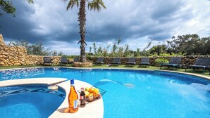 A swimming pool with lounge chairs and a stone wall. - Villa Soldanis Sleeps 12 with Pool (Xaghra)