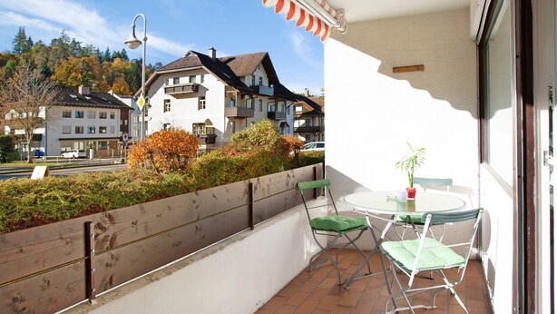 A balcony with a table and chairs, a view of buildings, and a street in the background. - Studio Apartment "Paulas" with Balcony and Wi-Fi (Füssen)