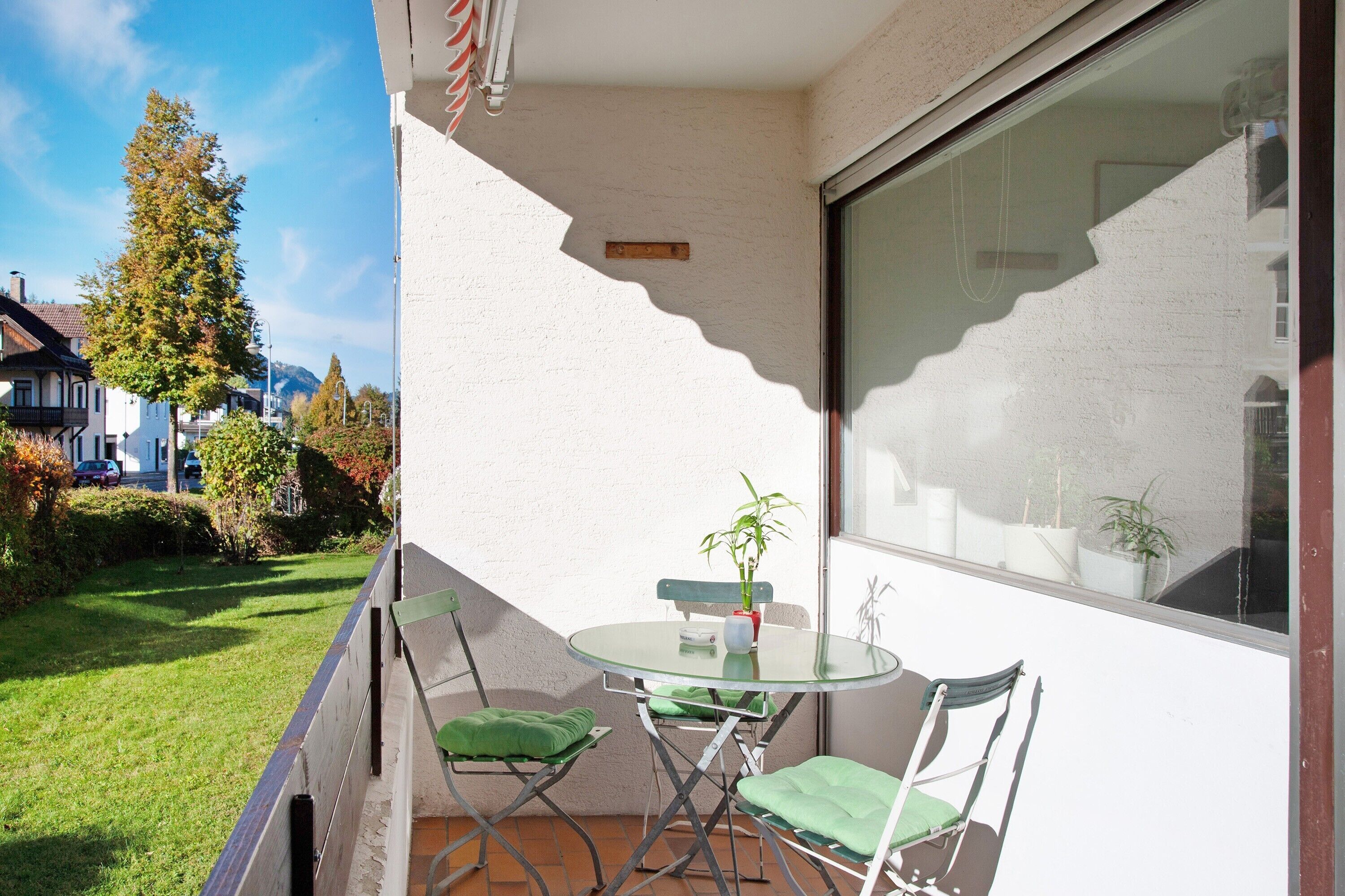Ein Balkon mit Glastisch und Stühlen, einem Blumentopf und Blick auf die umliegende Nachbarschaft.