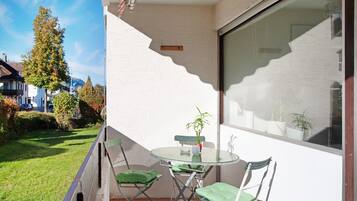 Ein Balkon mit Glastisch und Stühlen, einem Blumentopf und Blick auf die umliegende Nachbarschaft.