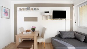 A modern living space with a dining table, chairs, a grey sofa, a flat-screen TV, and a shelf with decorative items. - Studio Apartment "Paulas" with Balcony and Wi-Fi (Füssen)