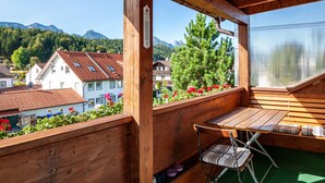 Un balcon en bois avec une table et une chaise, donnant sur un quartier résidentiel et des montagnes.