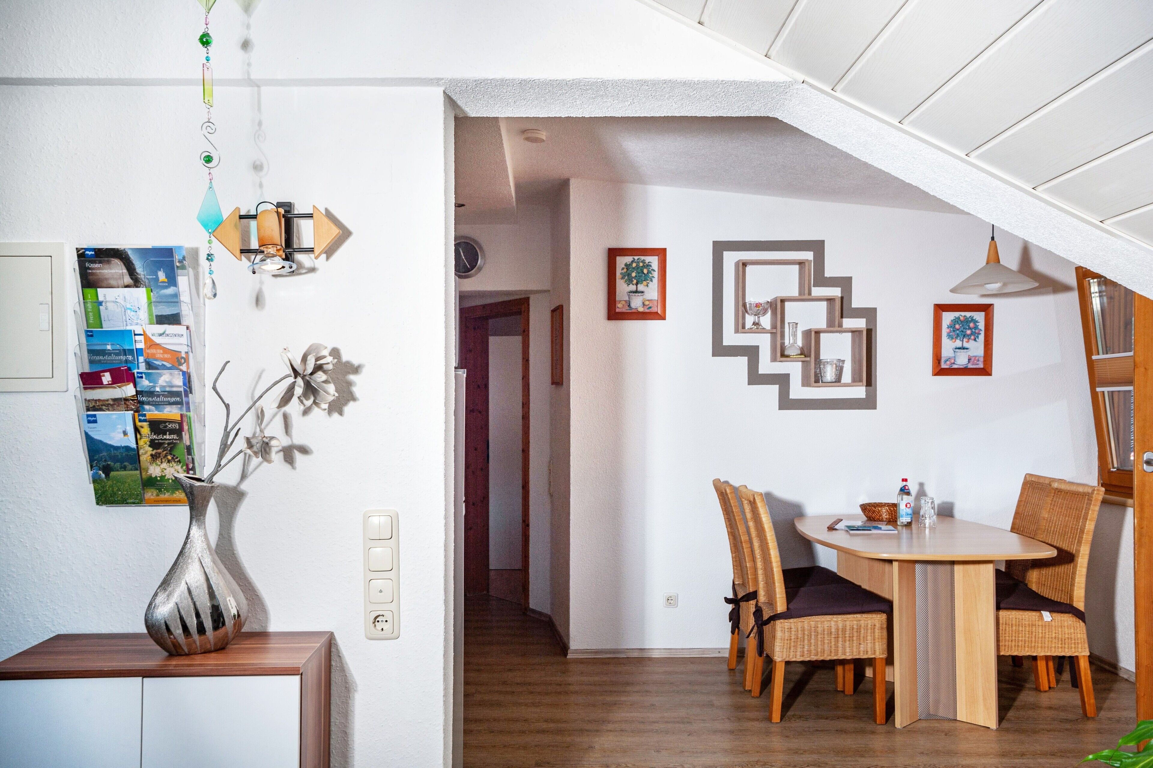 A dining area with a table and chairs, a vase with flowers, and a wall with framed pictures.