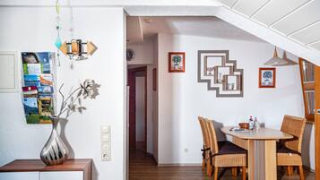 A dining area with a table and chairs, a vase with flowers, and a wall with framed pictures.
